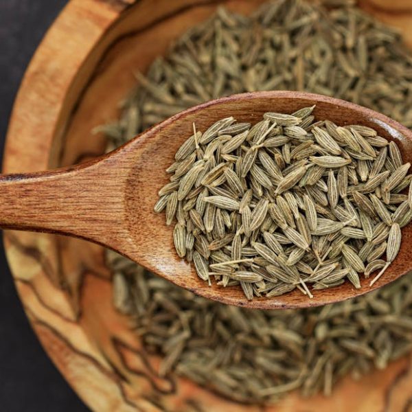 Detailed image of cumin seeds on a wooden spoon for culinary use.